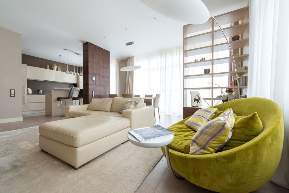 Stylish comfortable armchair with pillows placed near sofa in spacious living room in contemporary apartment